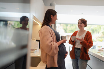 Pregnant woman talking to friend and drinking tea in kitchen