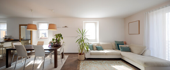 Front view of living room with a large sofa with cushions, table with leather chairs. Bright windows in a modern apartment