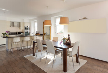 Open space with leather table and chairs and a modern kitchen with island and stools in the background
