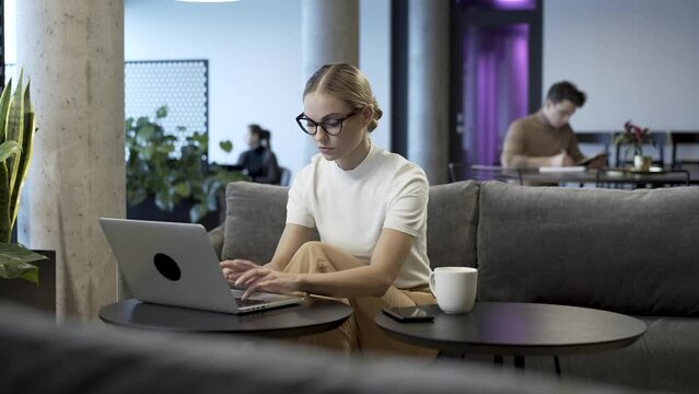 Young, beautiful and attractive business woman is finishing her daily work at modern co-working hub space. She typing in last changes on her project and press enter to send the completed file.