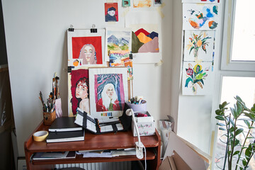Artist's studio with bright natural light, a lot of creative pictures and artistic tools at the table