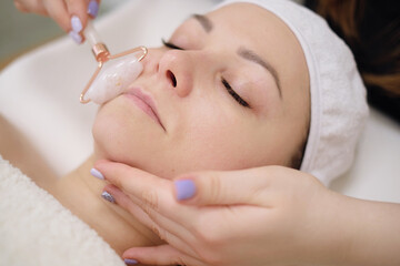 Calm patient woman undergoing the cosmetic facial massage procedures. Woman in salon making beauty treatment with gua sha stone