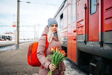 girl on the platform of the station with a red backpack and a bouquet of tulip flowers