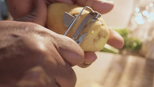 Close up shot of male African American hands peeling the potato with a metal peeler.