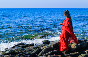 Young women wearing a red saree on the beach. Girl in traditional Indian sari among the rocks and...