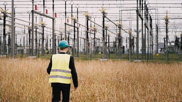 Electric engineer wearing helmet suit and safety vest walking towards substation 