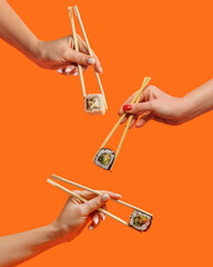 Women's hands hold sushi rolls with sticks. Orange background. Creative concept