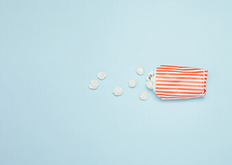 Flowers falling out of paper popcorn bag against pastel blue background. Minimal creative food concept. Space for copy.