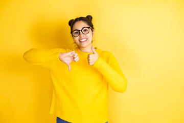 Young beautiful woman wearing casual sweater over isolated yellow background Doing thumbs up and down, disagreement and agreement expression. Crazy conflict