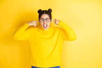 Young beautiful woman wearing casual sweater over isolated yellow background covering ears with...