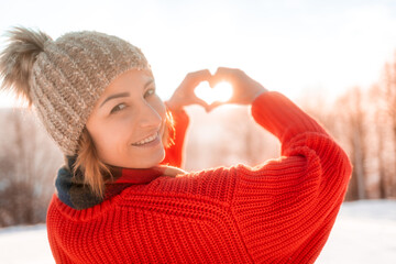 Smiling pretty girl in winter time making heart shape by hands