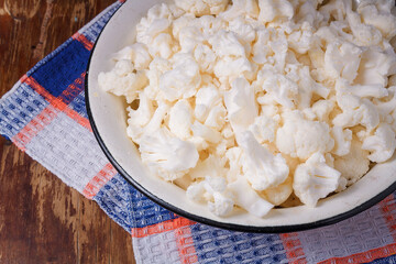 Bowl of cauliflower inflorescences on towel, wooden background. Organic farm vegetables, seasonal harvest, healthy eating, vegan diet.