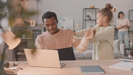 Medium shot of African American 8 year old girl asking her father trying to work on laptop from home to play with her and mans wife calming her down saying not to distract dad from work