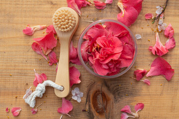 A natural wooden cosmetic brush on a wooden background surrounded by pink fresh flower petals. 