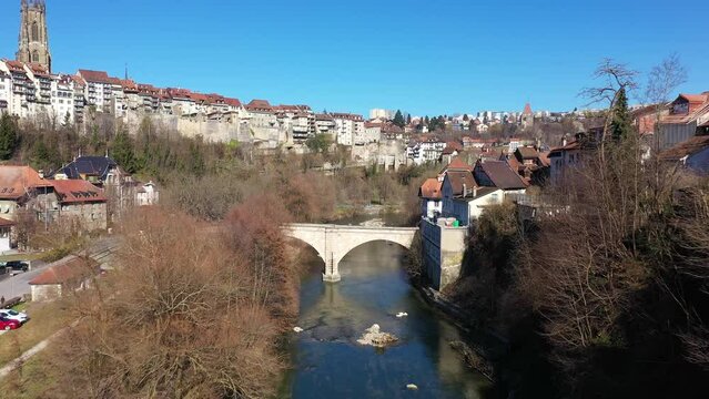 Aerial drone footage of the Fribourg medieval old town along the Sarine river in Switzerland on a sunny winter day with the old Saint Jean stone bridge with a forward motion. 