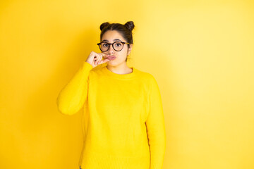 Young beautiful woman wearing casual sweater over isolated yellow background mouth and lips shut as zip with fingers. Secret and silent, taboo talking