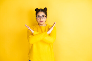 Young beautiful woman wearing casual sweater over isolated yellow background Rejection expression crossing arms doing negative sign, angry face