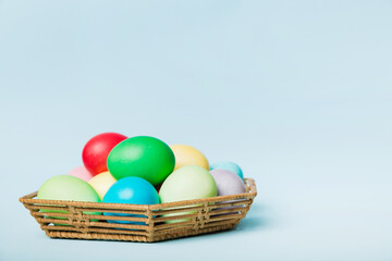 Multi colors Easter eggs in the woven basket on colored background . Pastel color Easter eggs. holiday concept with copy space