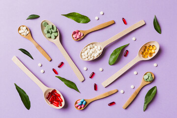 Top view Variety of vitamin and mineral pills in wooden spoon on Colored background. Top view of...