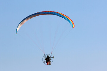 Paramotor pilot flying in a blue sky	