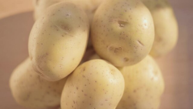 Heap of white potatoes, raw unpeeled plant tubers, spinning on a wooden plate, macro shot from above.