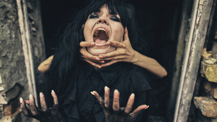 Emotional woman witch in black strangling hands she shouts