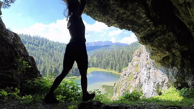 A woman walking out of a dark cave (Drachenhoehle) above the Sackiesensee in the Hochschwab mountain region, Styria, Austria. Slow motion. Concept. Freedom. Panoramic view in the Alps in Europe.
