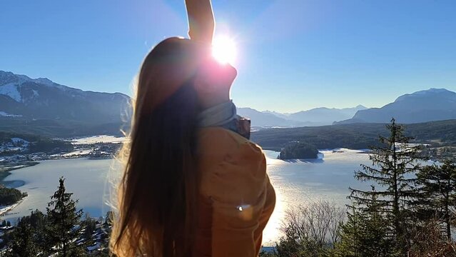 A woman flipping her hair with a scenic view on Faak lake in Carinthia, Austrian Alps. Slow motion. The picturesque lake is surrounded by high mountains. City of Villach tourism. Happiness concept.