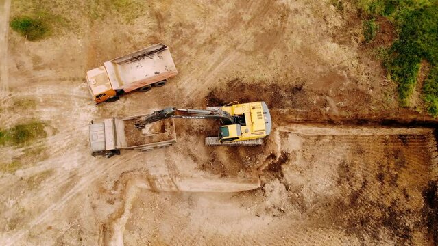 Top aerial shot: tractor bucket is filling a truck body. A excavator and truck are loading soil. Preparing place to construction residential house.