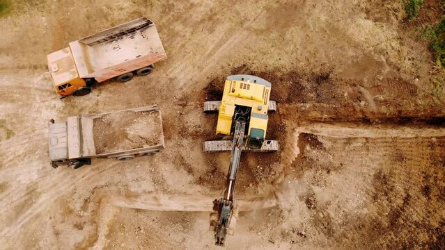 Aerial top down view of an excavator loading crushed stone into a dump truck in a crushed stone quarry. Excavator loading dump truck tipper at excavation site.