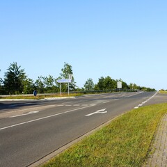 View of empty road in Itzehoe, Germany with traffic direction sign to Hamburg and trees in clear blue sky background. No people.