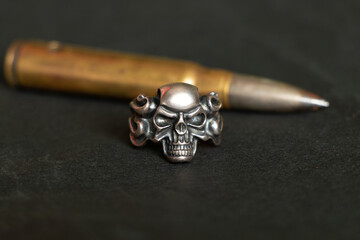 Silver ring with a skull and a bullet on a dark background, death and fear and war, weapons