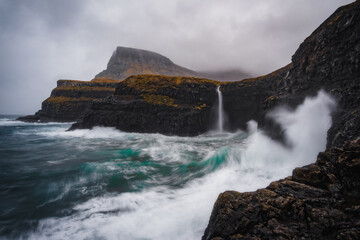 Dramatic view of Mulafossur waterfall with Gasadalur village on background. Vagar island, Faroe Islands, Denmark. November 2021.