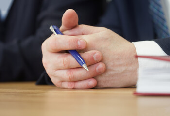 Folded hands of politician, deputy or businessman on the table along with pen. Official, boss,...