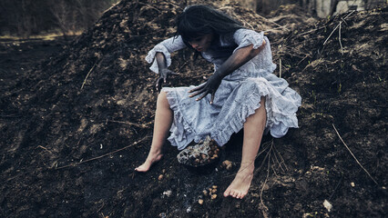 a witch with black hands in a white dress lies on the ground burning and screaming