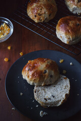 Close up angle view of Easter theme food image shot from above. Freshly baked and served on a plate hot cross buns. Ingredients and baking tray in shot. Copy space available. Dark and vintage style