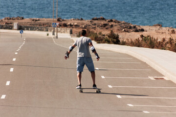 A man playing figure skating on a rural road in the sun on a bright day, Play surf skate near coast