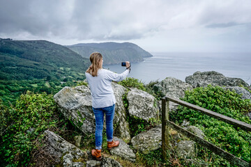 Naklejka premium Young and beautiful woman taking photos with the mobile on the coast of Galicia
