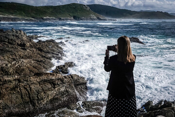 Young and beautiful woman taking photos with the mobile on the coast of Galicia