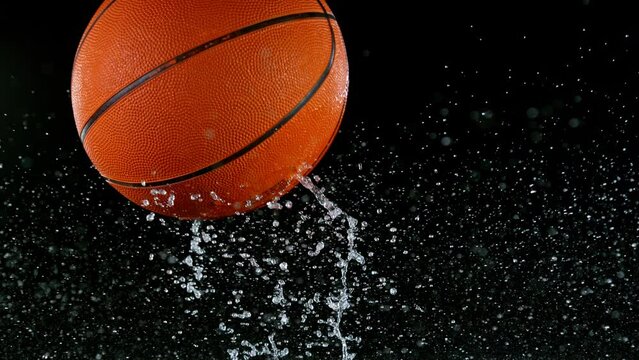 Super slow motion of falling basketball ball on water surface, black background. Filmed on high speed cinematic camera at 1000 fps.