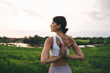 Back view of young Caucasian female in white top holding hands in namaste and thinking about inner...