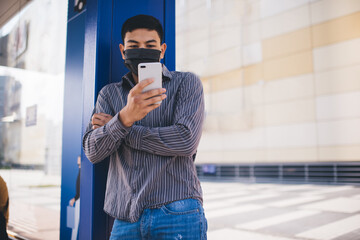 Guy in medical mask using smartphone on bus stop