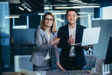 Two architects team, looking at camera and rejoicing smiling over completed project, keep thumbs up...
