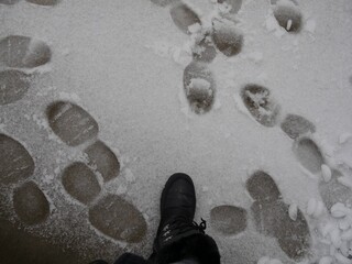 Fototapeta na wymiar Boot prints in the snow with a big black boot stepping on ice