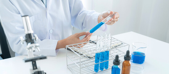 Scientist woman holding test tube in his hands and checking blue liquid from test tube while working