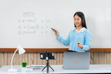 Female tutor standing in front of whiteboard and writing math equations on board to explaining new...