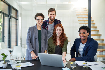 Were moving the company head-on towards success. Portrait of a group of young creatives working together on a laptop in a modern office.