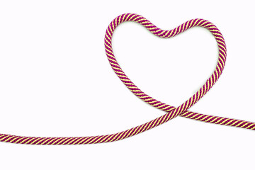 Multicolored rope in the shape of a heart on a white background. Red-yellow rope twisted in the shape of a heart on a paper background. Love concept or valentines day wedding decor