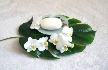 Body care and spa concept background with white organic soap and orchid flowers arranged on a philodendron leaf