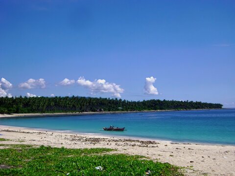 Blue waters of a tropical beach with a boat heading out to see Davao Oriental, Philippines.